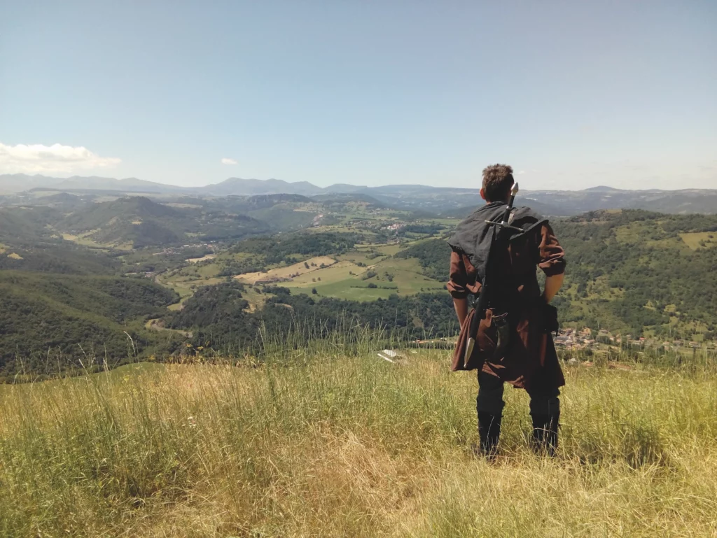 Homme déguisé en chevalier médiéval admirant le panorama sur les monts d'Auvergne près du château de Murol