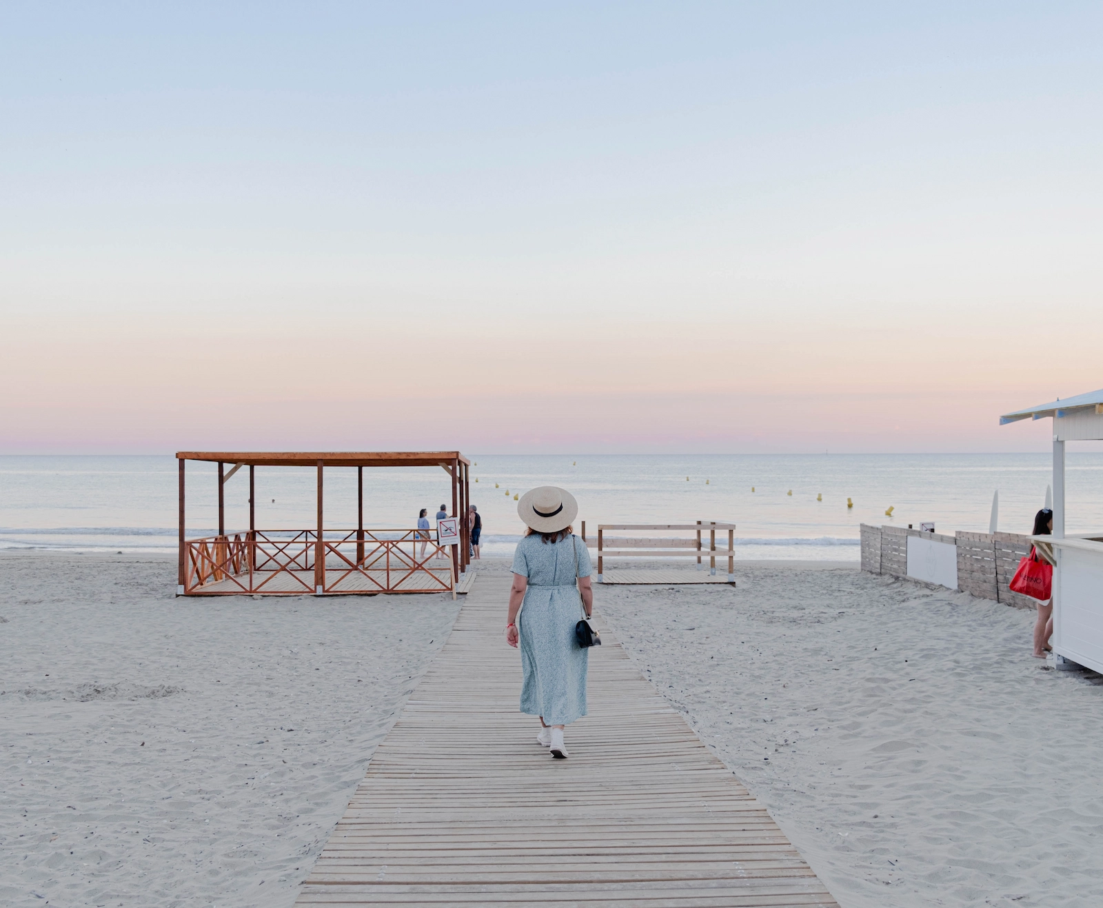 Femme en robe d'été marchant sur un ponton de bois vers la plage du Cap d'Agde au coucher du soleil